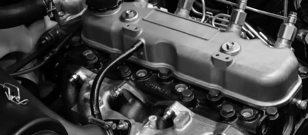 Diesel Repair near me in New Oxford, PA. A close-up view of a car engine in black and white, showing the intricate details and components, including bolts, hoses, and metallic surfaces. The focus is on the central part of the engine, highlighting the craftsmanship and mechanical complexity.