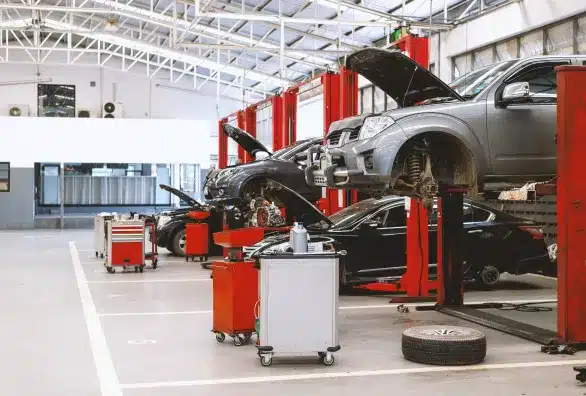 An auto repair shop with several cars elevated on hydraulic lifts. Open car hoods reveal ongoing servicing, while various red and white tool carts are scattered around.