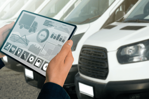 Fleet maintenance and repair in New Oxford, PA. Hands holding a tablet displaying data charts in front of white delivery vans lined up in a row.