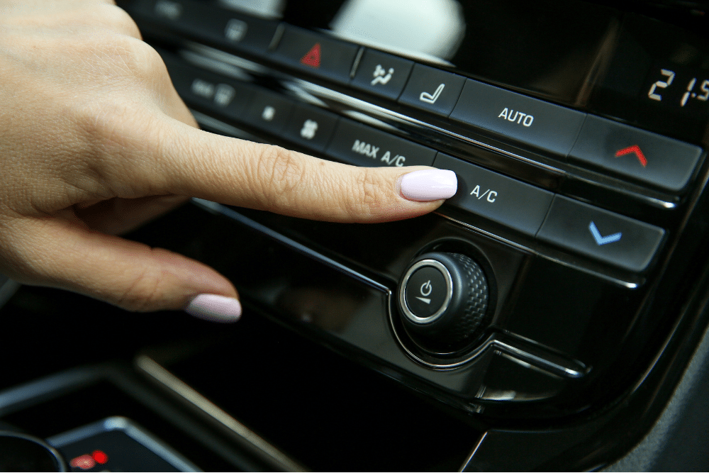 car a/c problems, Auto repair in New Oxford, PA at Premier Auto Works Inc. Close-up of a person’s hand pressing the A/C button on a modern car climate control panel.