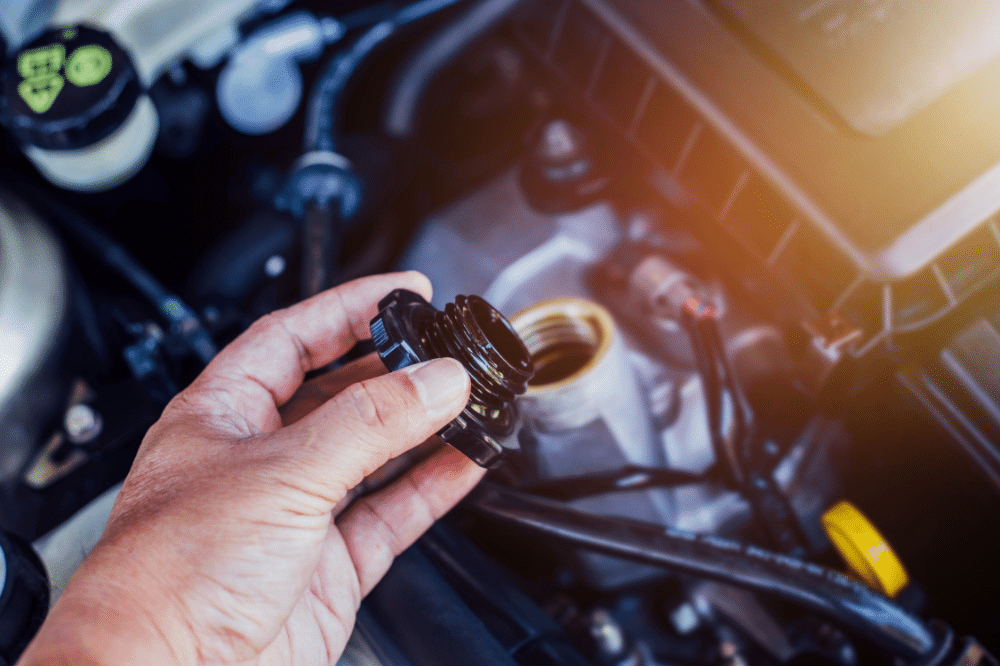 transmission fluid, Auto repair in New Oxford, PA at Premier Auto Works Inc. A person’s hand unscrewing the engine oil cap in a car engine bay, preparing for an oil check or fill.