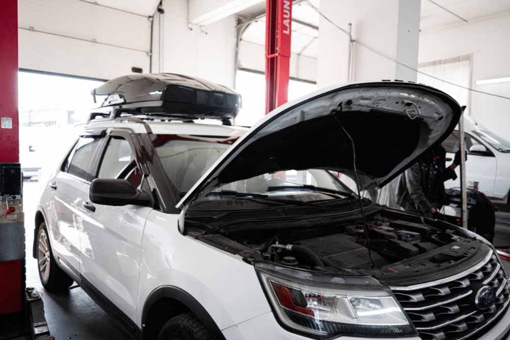 Ford Repair, Auto repair in New Oxford, PA at Premier Auto Works Inc. White SUV with its hood open inside an auto repair shop, showing the engine compartment. A roof cargo box is mounted on top of the vehicle.