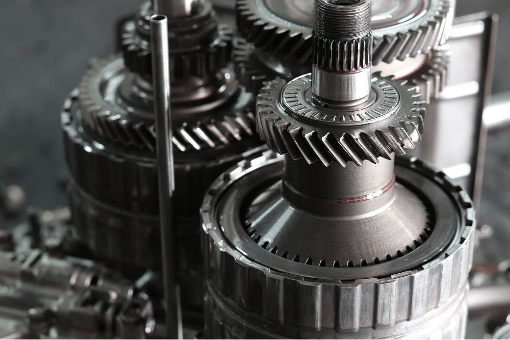 Transmission Failure in New Oxford, PA at Premier Auto Works Inc. A close-up of a metal automotive component, likely a pump or bearing assembly, resting on a workbench. The central shaft protrudes outward, surrounded by a circular seal with visible oil residue and grime. Several mounting bolt holes and fasteners are built into the housing, which shows signs of wear and light corrosion.
